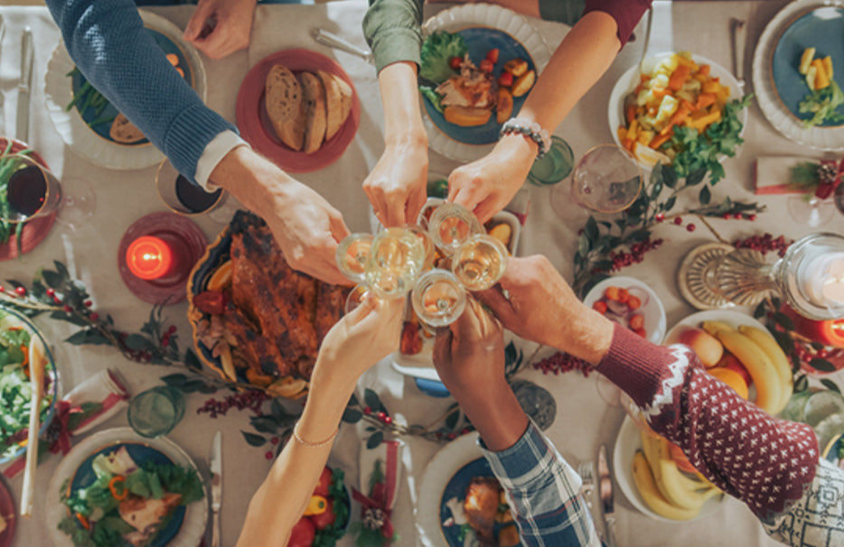 Pohled shora na slavnostně prostřený zimní stůl, u kterého si několik lidí připíjí skleničkami.
